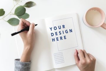 Birds eye view of desk with person designing logo on notebook